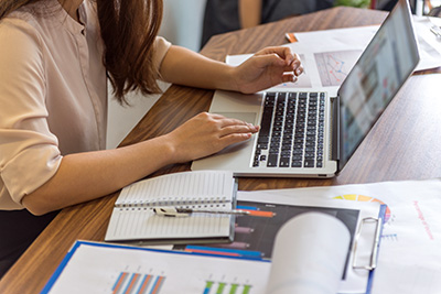 Woman using laptop on desk with notebook and papers