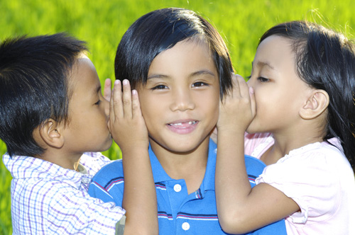 two boys whispering to another boy