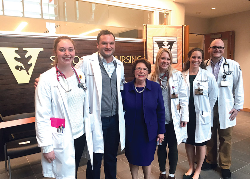 Dean Linda Norman with students and faculty in front of wood wall in VUSN atrium