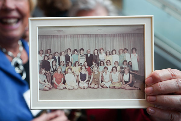In 2019, a woman holds a framed photo of her fellow Class of 1969 classmates