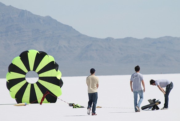 Students view rocket lying on the ground with parachute fluttering.