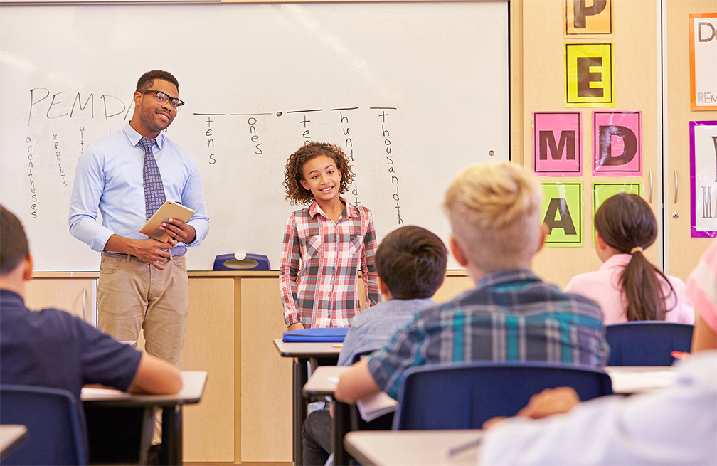 teacher standing by student as she presents in front of class