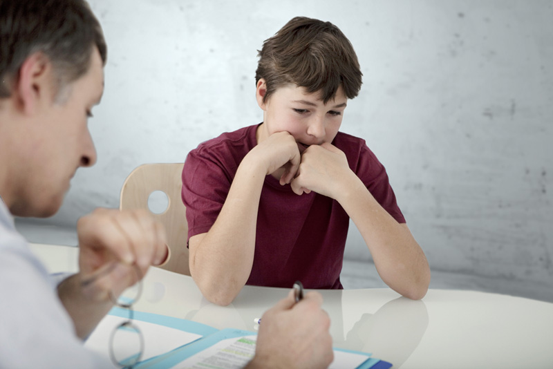 boy at table watching adult read paper