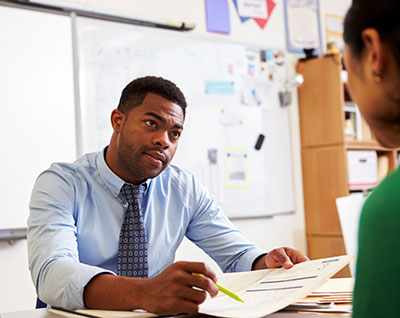 teacher at desk confering with student