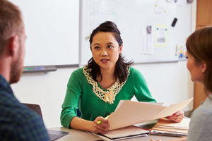Woman at desk holding papers while talking to man and woman
