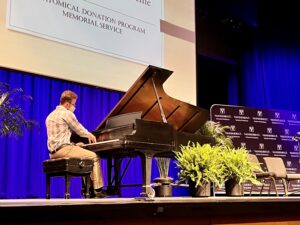 A man in khakis plays a black grand piano