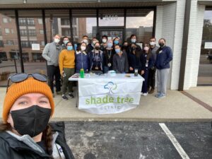 A woman in a mask takes a selfie with a group of medical volunteers standing behind a table