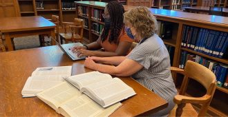 librarian and student work at desk with laptop and books