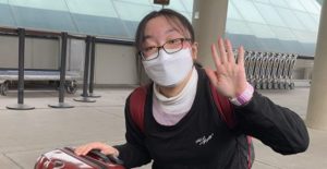 masked student waving in airport