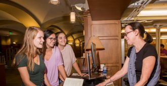 Librarian works with three students at the reference desk