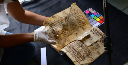 fragile, falling apart old book being positioned for scanning by gloved hands