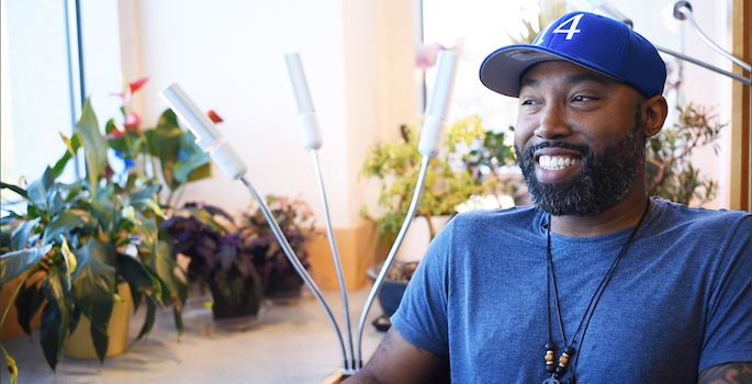Steven Townsend wearing t-shirt and baseball cap sitting in his office which is full of plants
