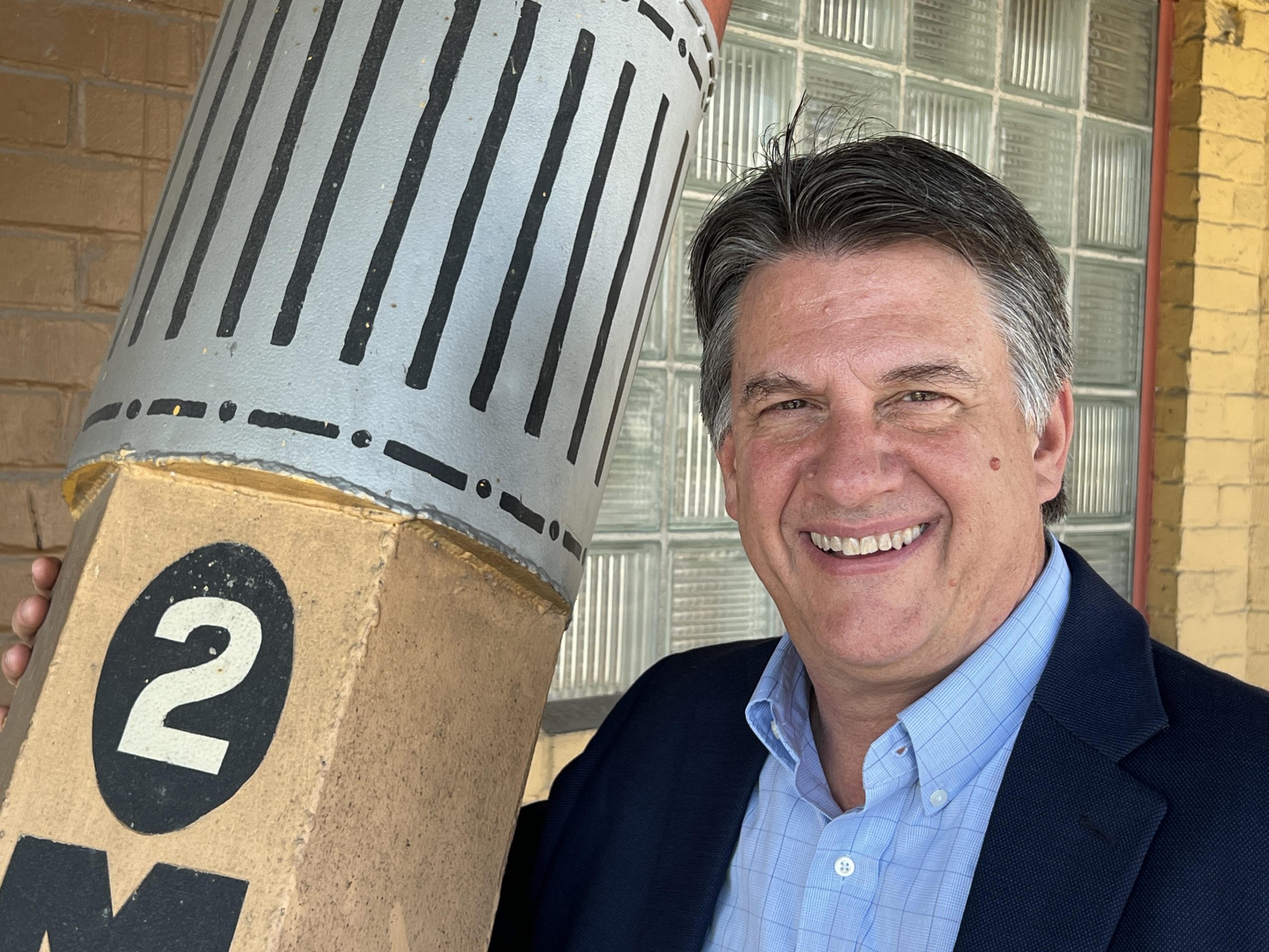 Photo of alumnus Scott Johnson, standing next to a very large mockup of a No. 2 yellow pencil at Musgrave Pencil Company