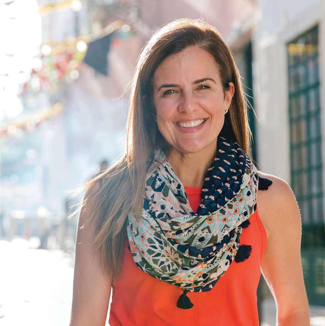 Color portrait of Nicole Feliciano in orange blouse and white pants on a city street