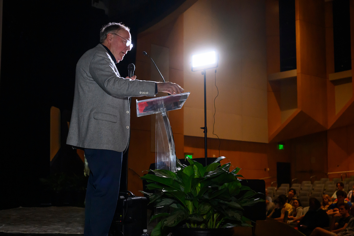 James Patterson stands before a podium and speaks to an auditorium of people