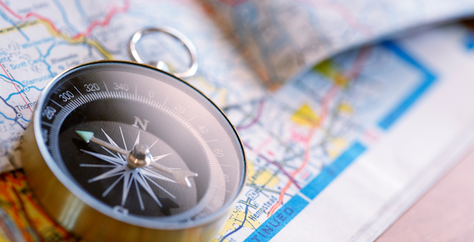A compass sits on top of a road map. The image is captured using a very shallow depth of field.