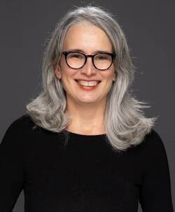 woman with silver hair, glasses, and wearing black long-sleeved blouse