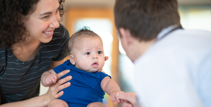 A mother holds her son in her arms while a male doctor gives him a checkup.