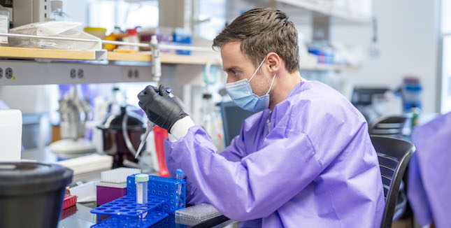 Student researchers wears face mask and gloves while conducting experiment in lab at the Engineering Science Building