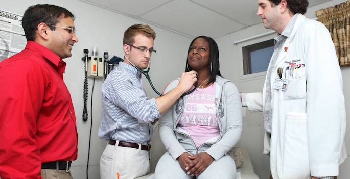 three medical practitioners with patient in exam room
