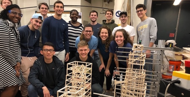 Civil engineering students pose behind a project where they built and tested balsa wood towers