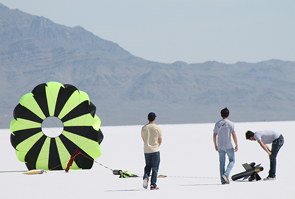 Students view rocket lying on the ground with parachute fluttering.