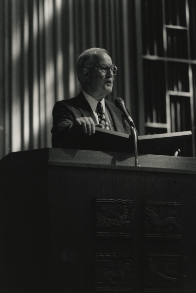 Black/white photo of a man in a suit at the lectern of Benton Chapel at Vanderbilt with rays of light on the wall behind him