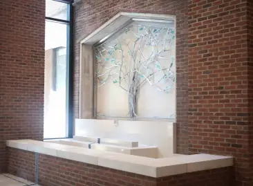 The focal point upon entering is a commissioned tree sculpture and water wall, symbolizing growth and universal connection. Framed by an existing masonry arch, the tree is composed of stainless steel, with its leaves crafted of copper salvaged from one of the former side entrances. (Susan Urmy/Vanderbilt)