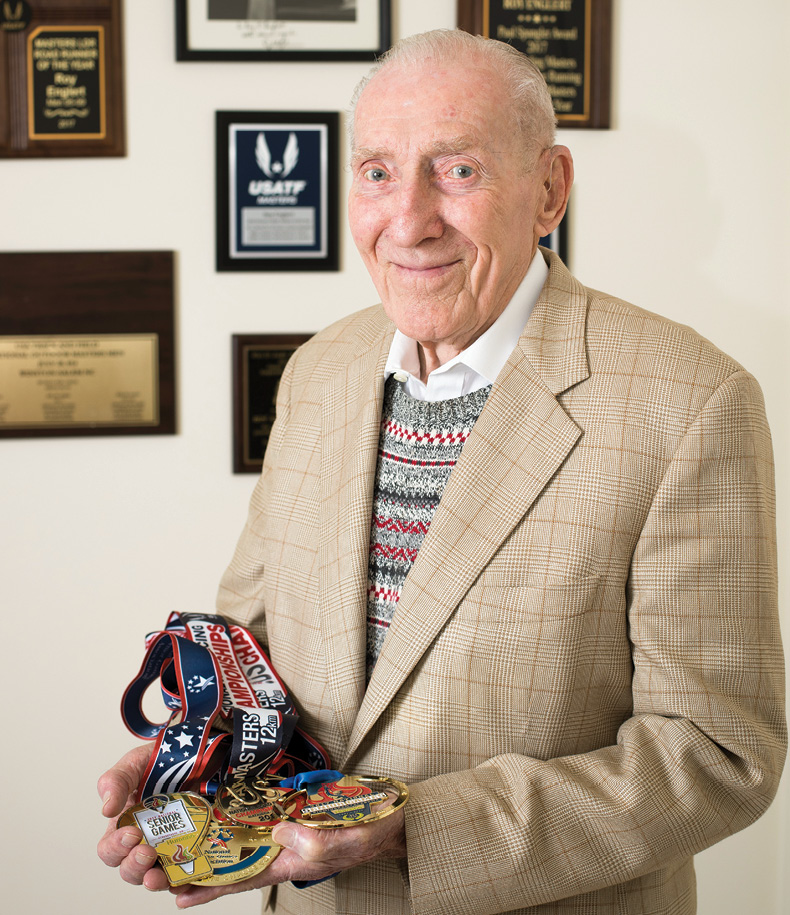 photo of Roy Englert holding several of his running medals