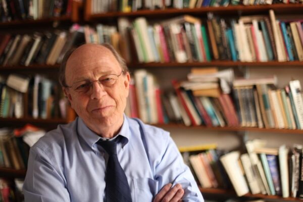 photograph of Vereen Bell wearing blue shirt and tie, sitting in front of crowded book shelf