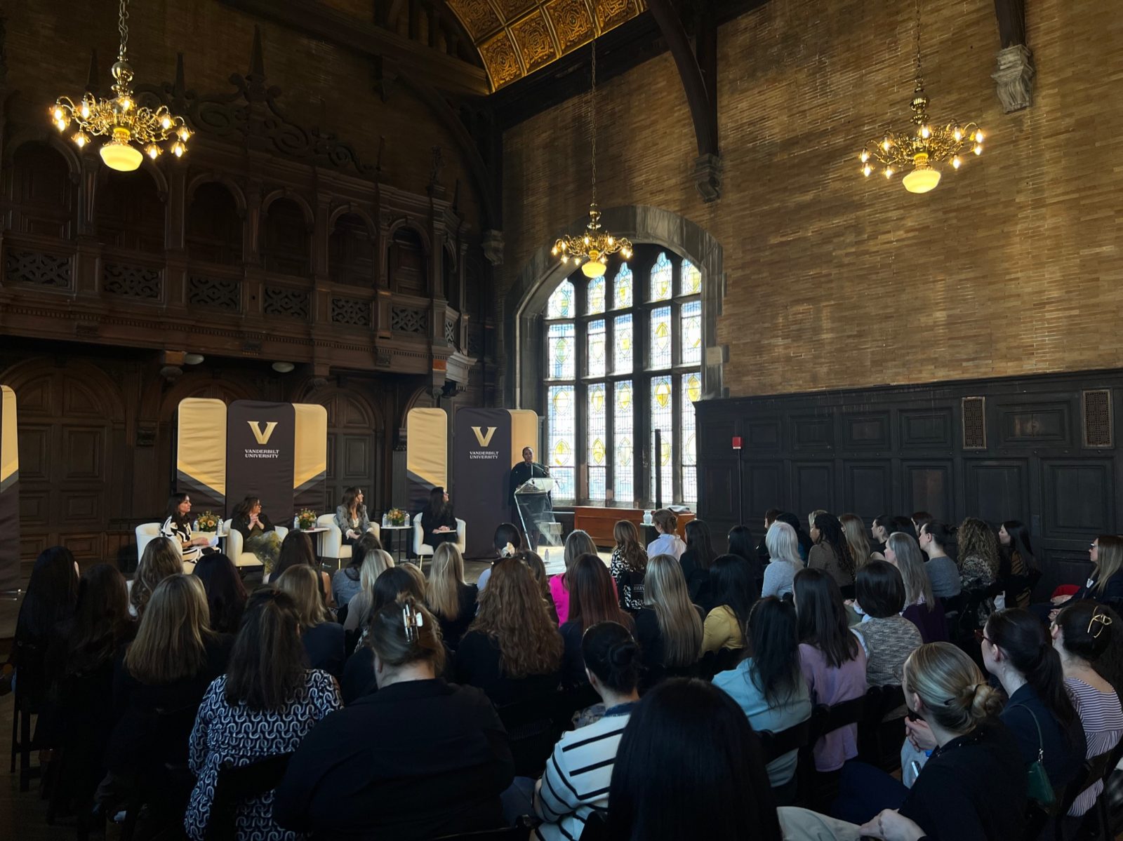 Image Description: Attendees sitting and listening to speakers on a stage. 
