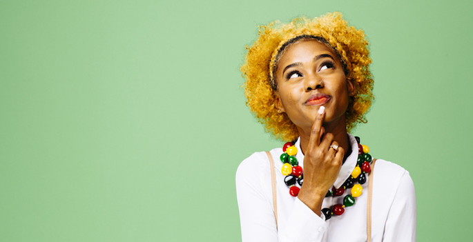 Young African American woman thinking and looking up, isolated on green studio background