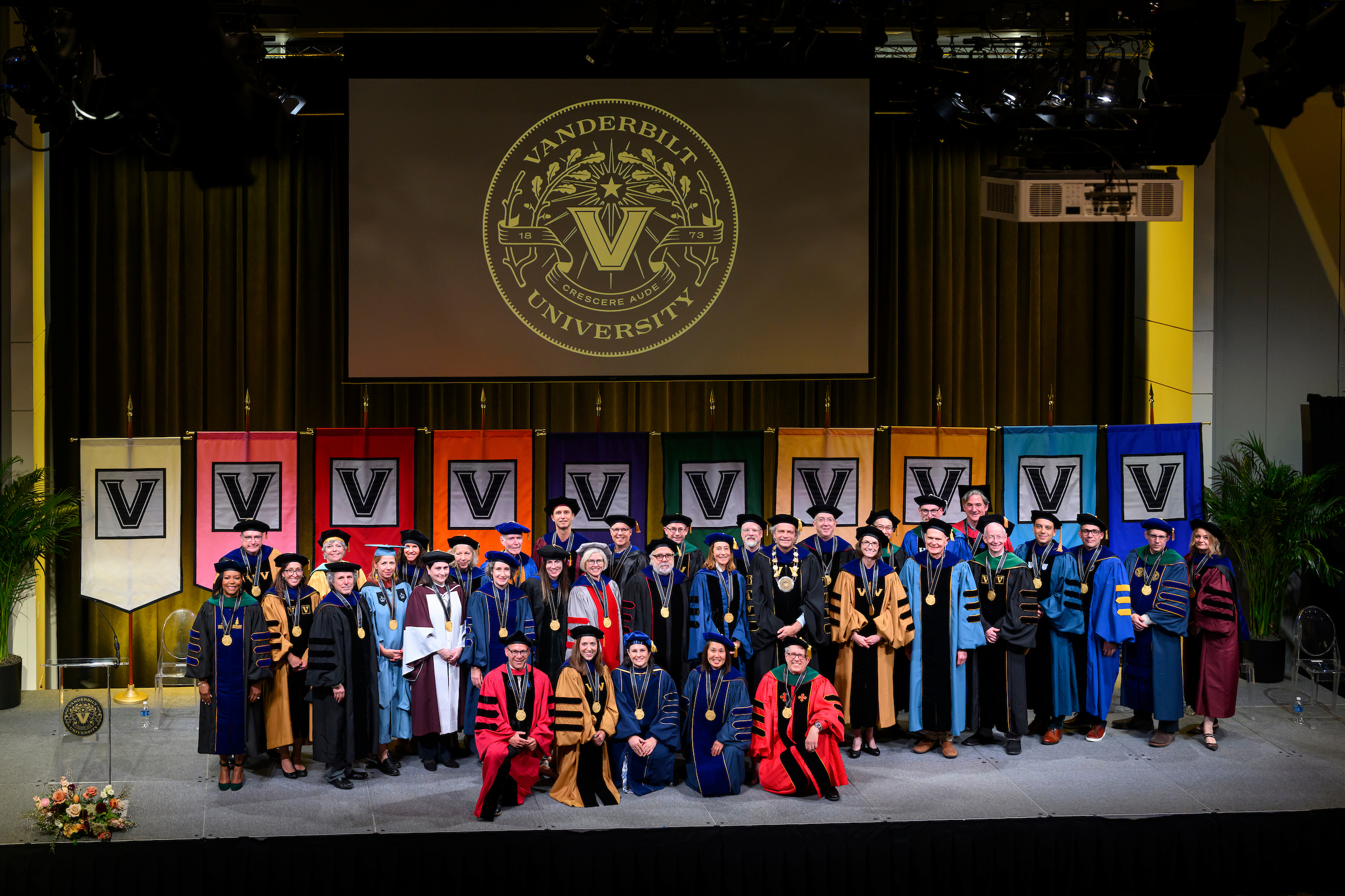 Endowed chairs in full regalia standing in a group photo before the Vanderbilt logo