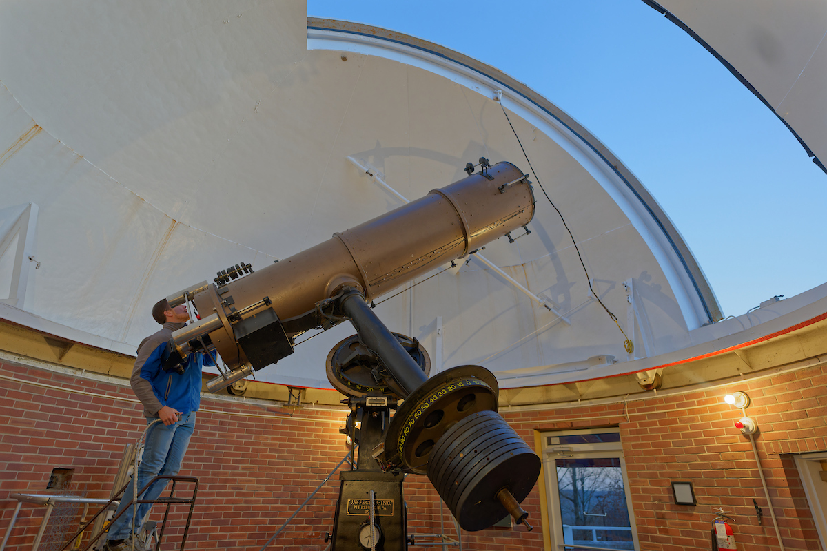A man standing behind a large telescope aimed at the sky