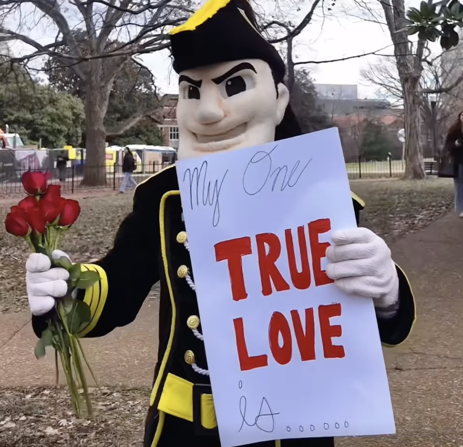 Mr. C holds a bouquet of roses and a sign that reads "My one true love is..."