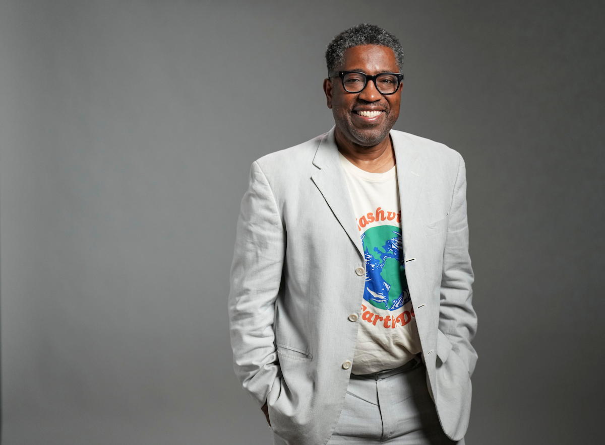 Major Jackson stands with his hands in his pockets, smiling against a gray wall