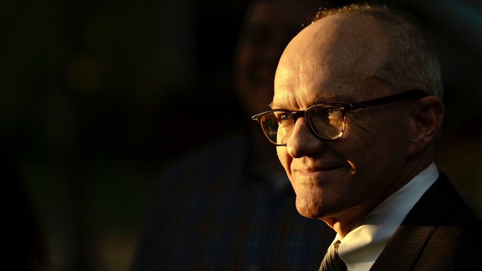 A man wearing glasses set against a black background.