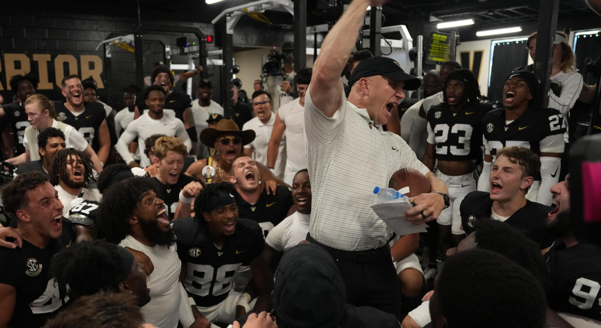 Football coach Clark Lea stands in the center of a crowd of players cheering a victory
