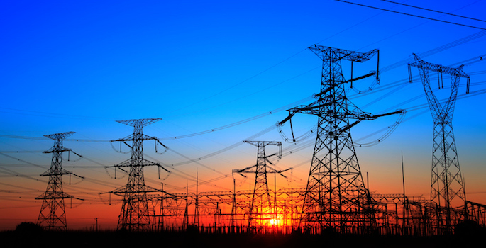 The silhouette of electricity transmission pylons at sunset