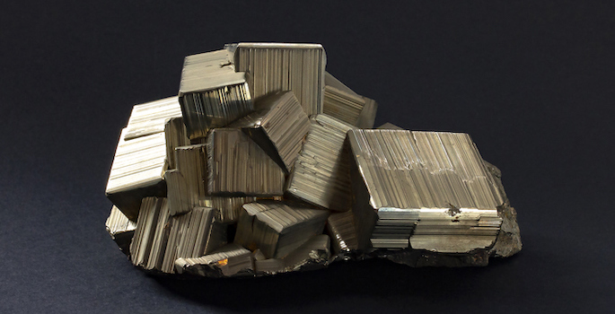 close up of gold-colored pyrite chunk, with several cube-like crystal protrusions, on black background