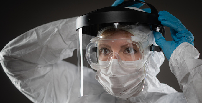 Female Medical Worker Wearing Protective Face Mask and Gear Against Dark Background.