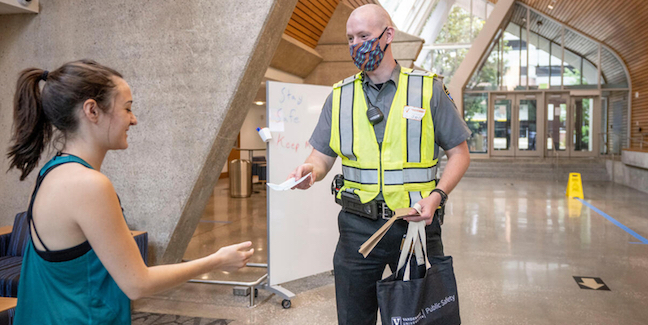 COVID Ambassador hands a face mask to a campus community member