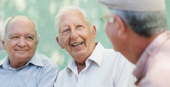 Active retirement, group of three old male friends talking and laughing on bench in public park
