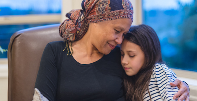 Asian senior woman with cancer holds her granddaughter tightly in her lap. Grandma is wearing a headscarf and smiling. (A beautiful ethnic senior woman with cancer holds her granddaughter tightly in her lap. Grandma is wearing a headscarf