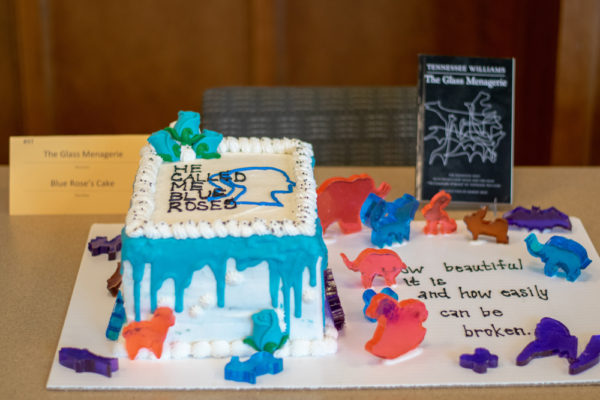 A white cake with blue icing and the quote "He called me blue roses" written in icing.