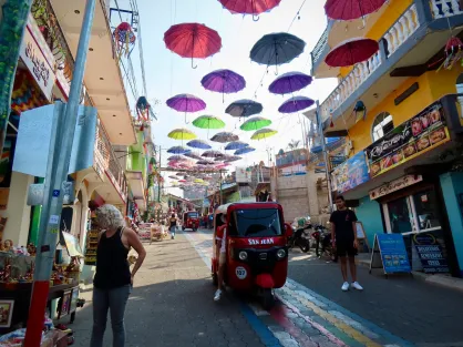 Isabella Bautista in Guatemala "Pictured here is a tuk-tuk — the Guatemalan version of a taxi — on a street in San Juan La Laguna, Sololá, Guatemala. San Juan is known for its artisan shops, where locals sell handmade crafts. In this photograph, tourists and natives alike browse the shops on a street shaded by colorful umbrellas and lined by motorcycles, one of the most highly preferred modes of transportation in Guatemala."
