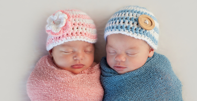 Five week old sleeping boy and girl fraternal twin newborn babies. They are wearing crocheted pink and blue striped hats.