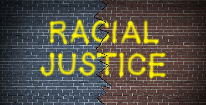 brick wall with 'racial justice' spray painted in yellow over a thick crack bisecting the middle of the wall