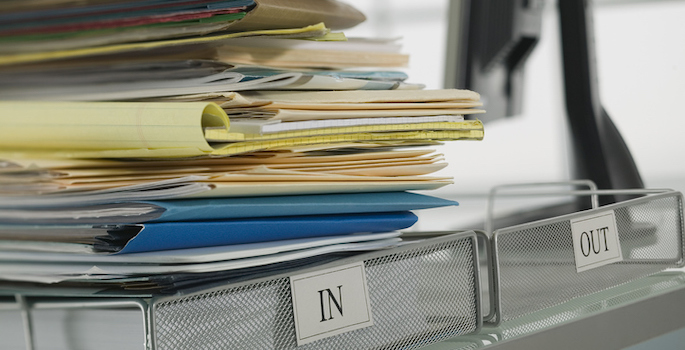 wire inbox overflowing with documents next to empty wire outbox