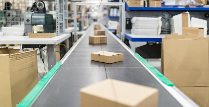 Cardboard boxes on moving belt conveyor at distribution warehouse. Modern warehouse with automatic moving conveyor machine.